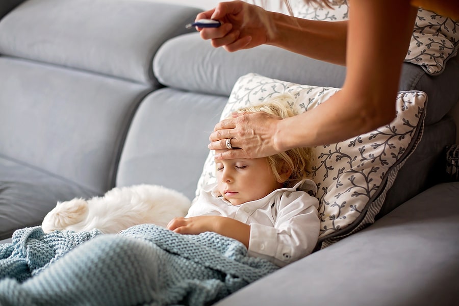 Moeder meet temperatuur van haar peuter die ligt op de bank