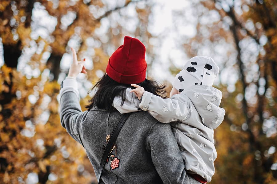 Moeder speelt met kindje in herfstbos en denkt na over de juiste polis