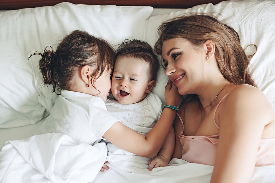 Baby 18 Wochen Mutter kuschelt mit ihren zwei Kindern im Bett