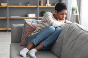 Schmierblutung: Frau sitzt zusammengekrümmt auf dem Sofa.