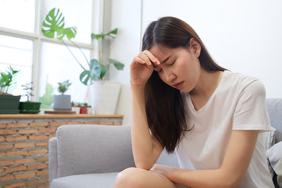 Asiatische Frau sitzt auf der Couch und fühlt sich nicht wohl.
