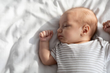 TOG: Baby liegt im Bett und schläft mit einem Body bekleidet