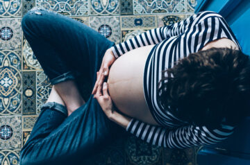 Was ist der Schleimpfrop? Schwangere Frau betrachtet ihren Babybauch.