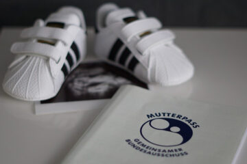 Kleine Babyschuhe liegen auf einem Mutterpass.