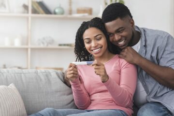 Pärchen sitzt auf der Couch und freut sich über positiven Schwnagerschaftstest