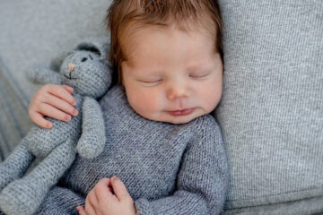 Mädchen oder Junge Säugling liegt auf grauer Decke mit einem grauen Hasen in der Hand und schläft