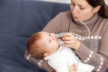 Mutter probiert mit einem Nasensauger die Nase ihres Babys frei zu bekommen