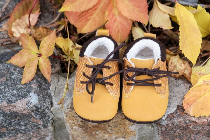 Gelbe Babyschuhe zwischen Herbstblättern.