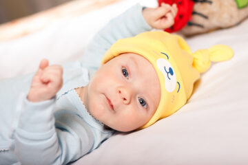 Neugeborenes Baby hat gelbeMütze auf und liegt auf dem Bett