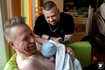Ein schwules Paar kuschelt mit ihrem Baby, dass von einer Leihmutter ausgetragen wurde.