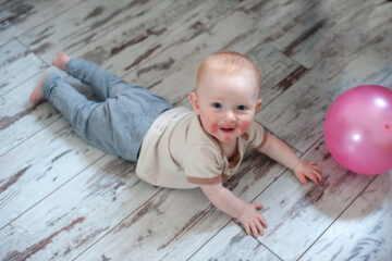 Baby mit Neurodermitis liegt auf dem Boden und spielt mit einem Luftballon