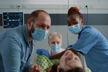 Schulterdystokie: Eine Schwangere liegt in den Wehen und wird von ihrem Partner und Geburtshelfern unterstützt.