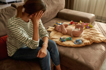 Mutter guckt müde zu ihrem Baby auf der Couch: wochenbettdepression