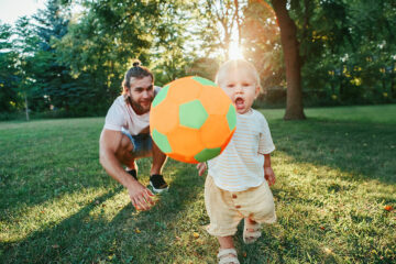 Vater spielt mit seinem Baby draußen Ball
