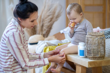 Mama verarztet ihr Baby mit einem Pflaster aus der Reiseapotheke.