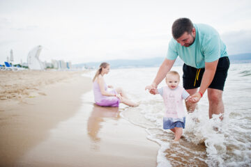 Eltern spielen im Urlaub mit Baby am Strand.