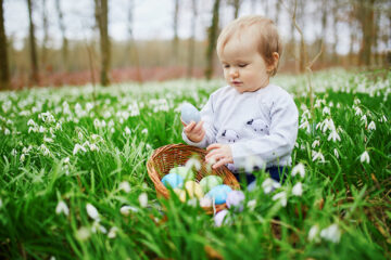 Ostergeschenke für Kinder: Baby sitzt mit Osternest im Gras.
