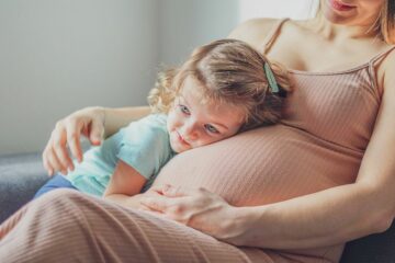 Zweite Schwangerschaft: Kleinkind kuschelt mit dem Babybauch ihrer Mama.