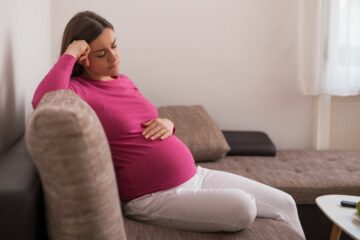 Schwangere Frau sitzt auf dem Sofa und hat Blähungen